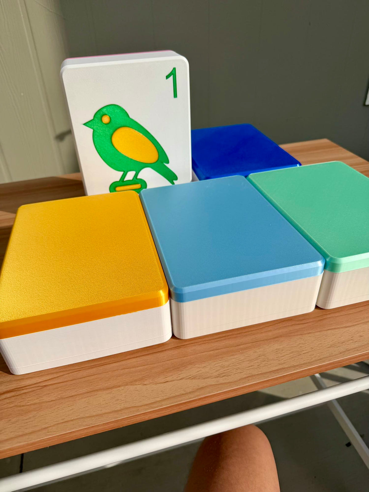 Colorful Spools mega tile display cases with the 1 bam bird lid, on a wooden table