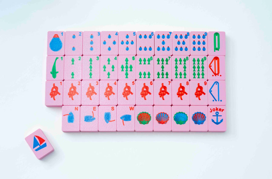 Pink Spools nautical mahjong tiles laid out in a grid: buoy dots, fish bams, knot cracks, dragons, winds, shell flowers, and an anchor joker, with one sailboat tile back