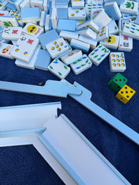 Close-up of the blue Travel Mahjong set by Spools, showing tiles, matching racks, pushers, and floating dice on a navy towel.