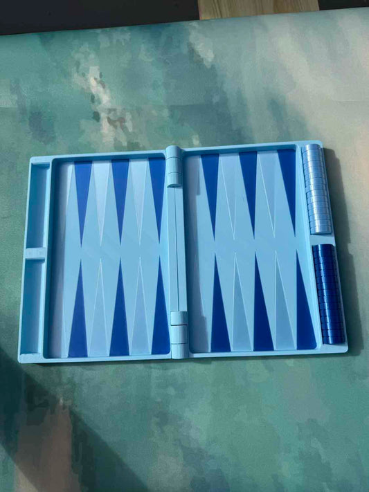 A blue and white backgammon board game set with dice cups, shown open on a textured green surface.
