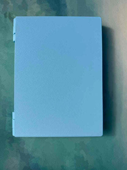 A light blue rectangular backgammon set with white rings on the left side, photographed from above on a textured green surface.